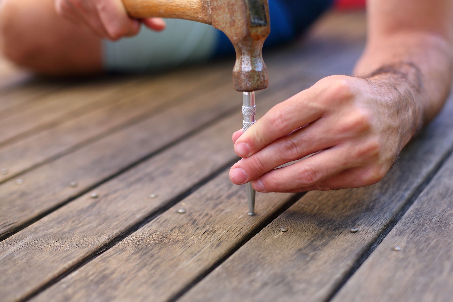 A man is hammering a nail into a wooden deck.