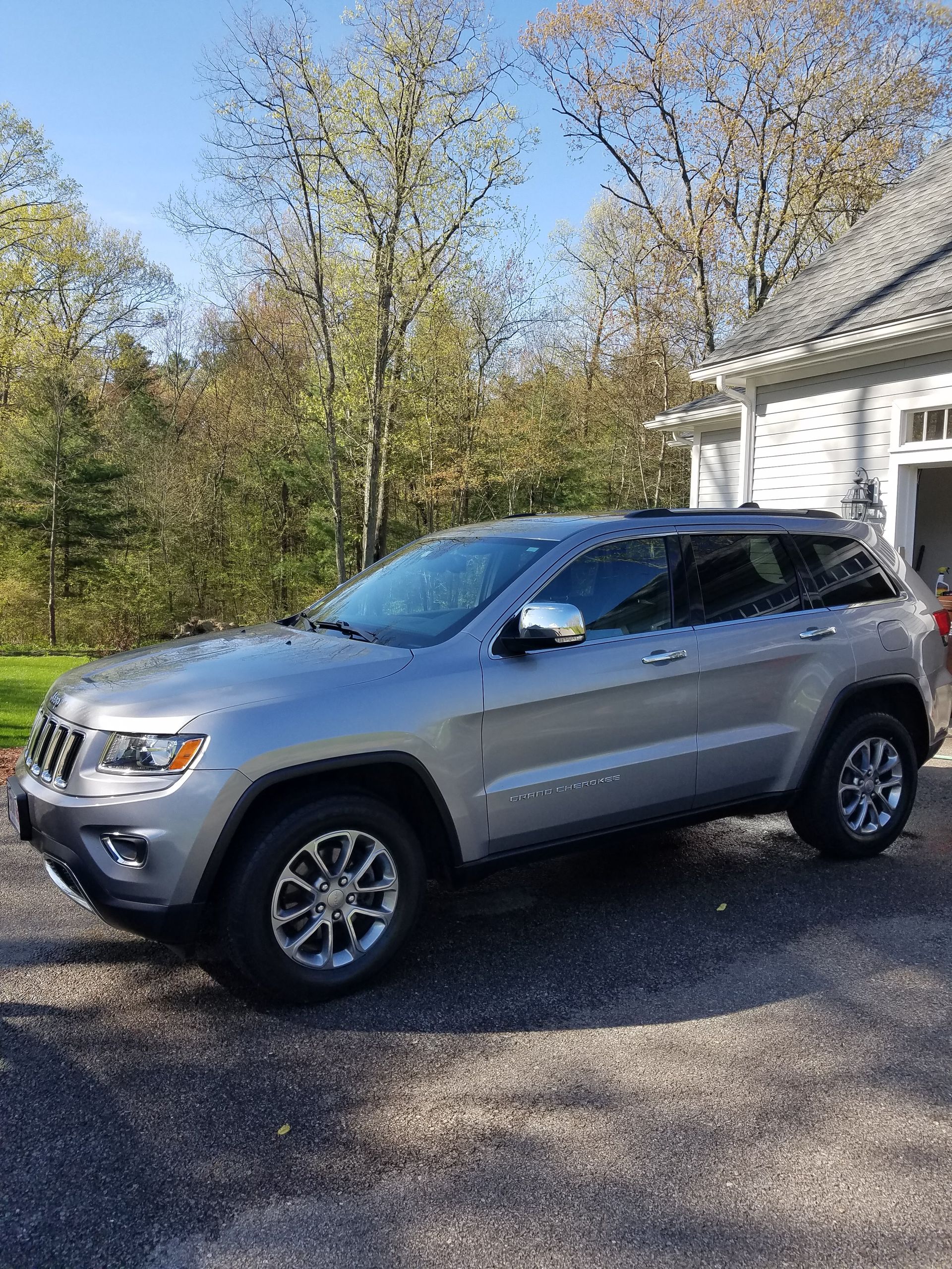 A silver jeep grand cherokee is parked in front of a house.