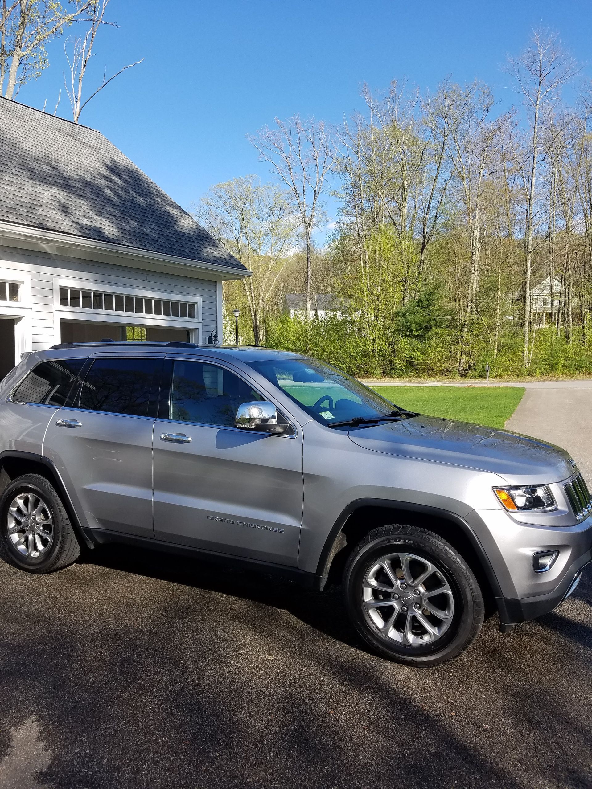 A silver jeep grand cherokee is parked in front of a garage.