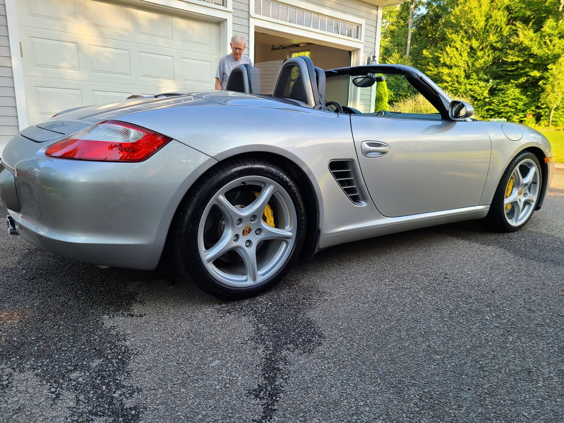 A silver porsche boxster is parked in front of a garage.