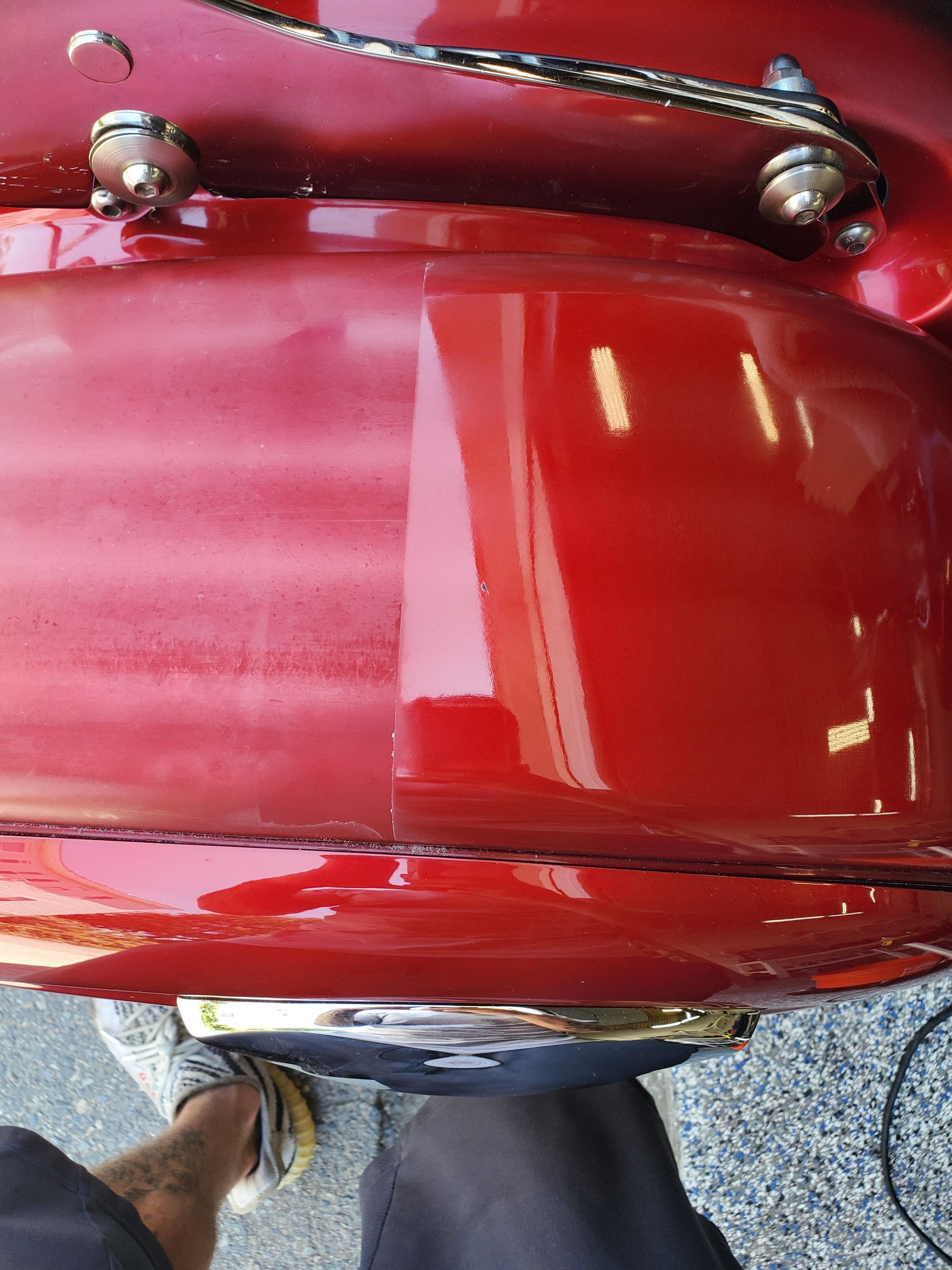 A person is standing next to a red motorcycle in a garage.
