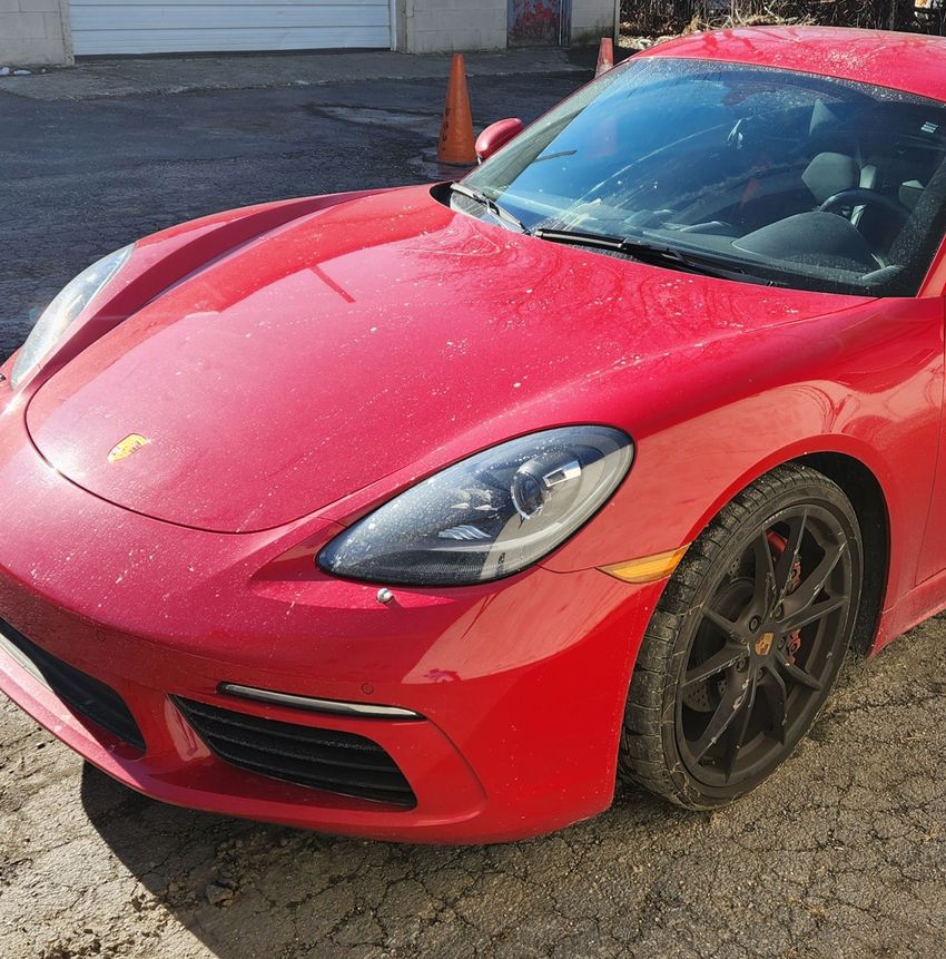 A red Porsche sports car parked on an outdoor pavement, shown from a front three-quarter angle.