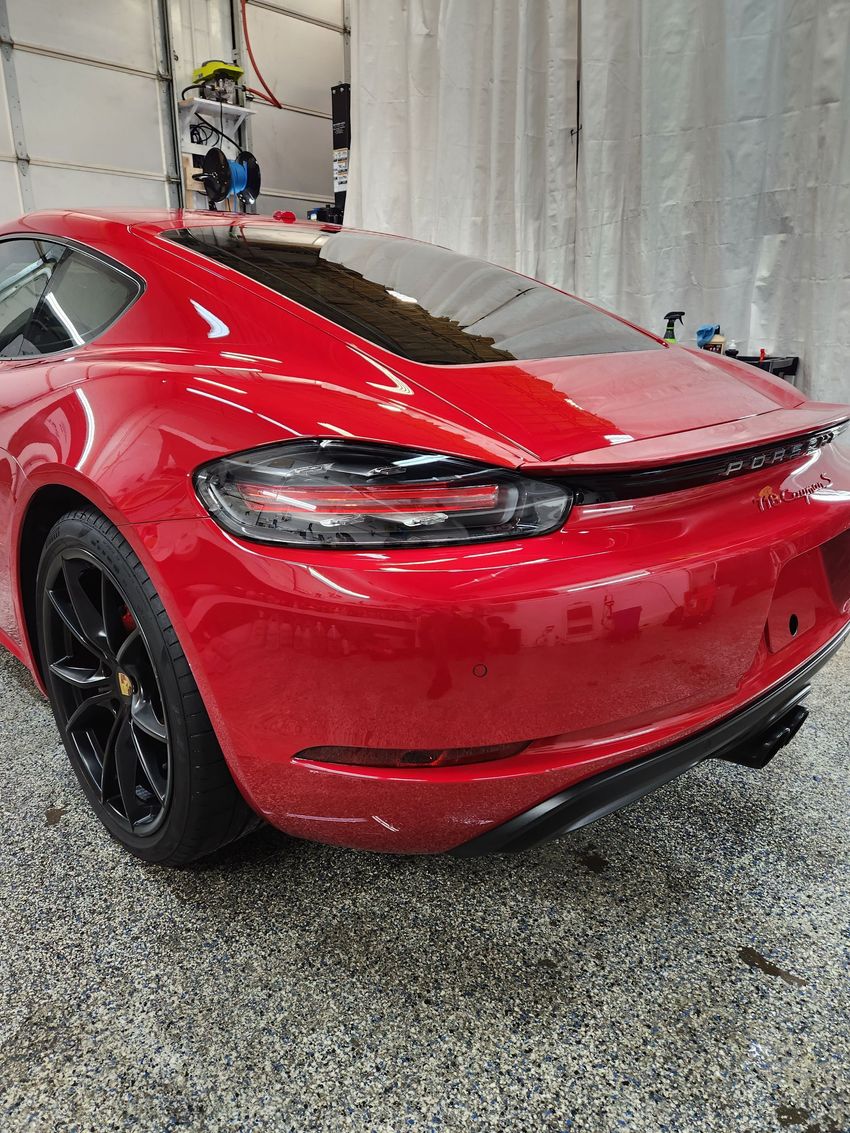 A shiny red Porsche sports car with black wheels parked inside a garage.