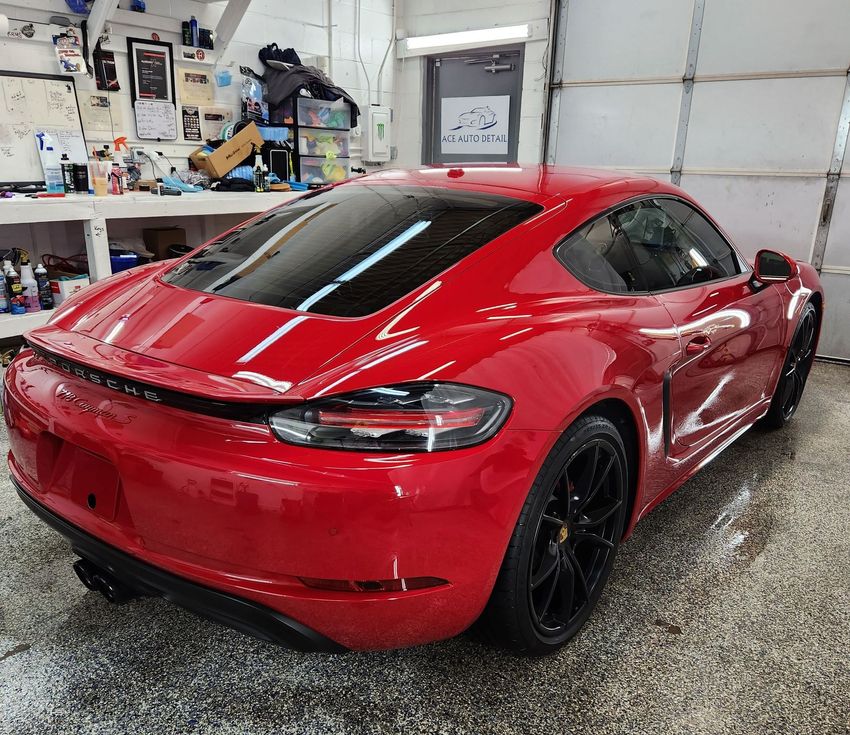 A shiny red Porsche sports car parked inside a well-lit, organized garage with a speckled floor.