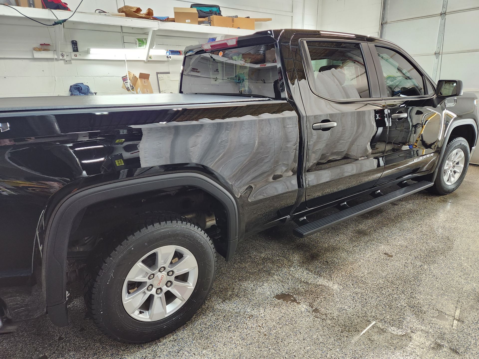 A black truck is parked in a garage next to a garage door.