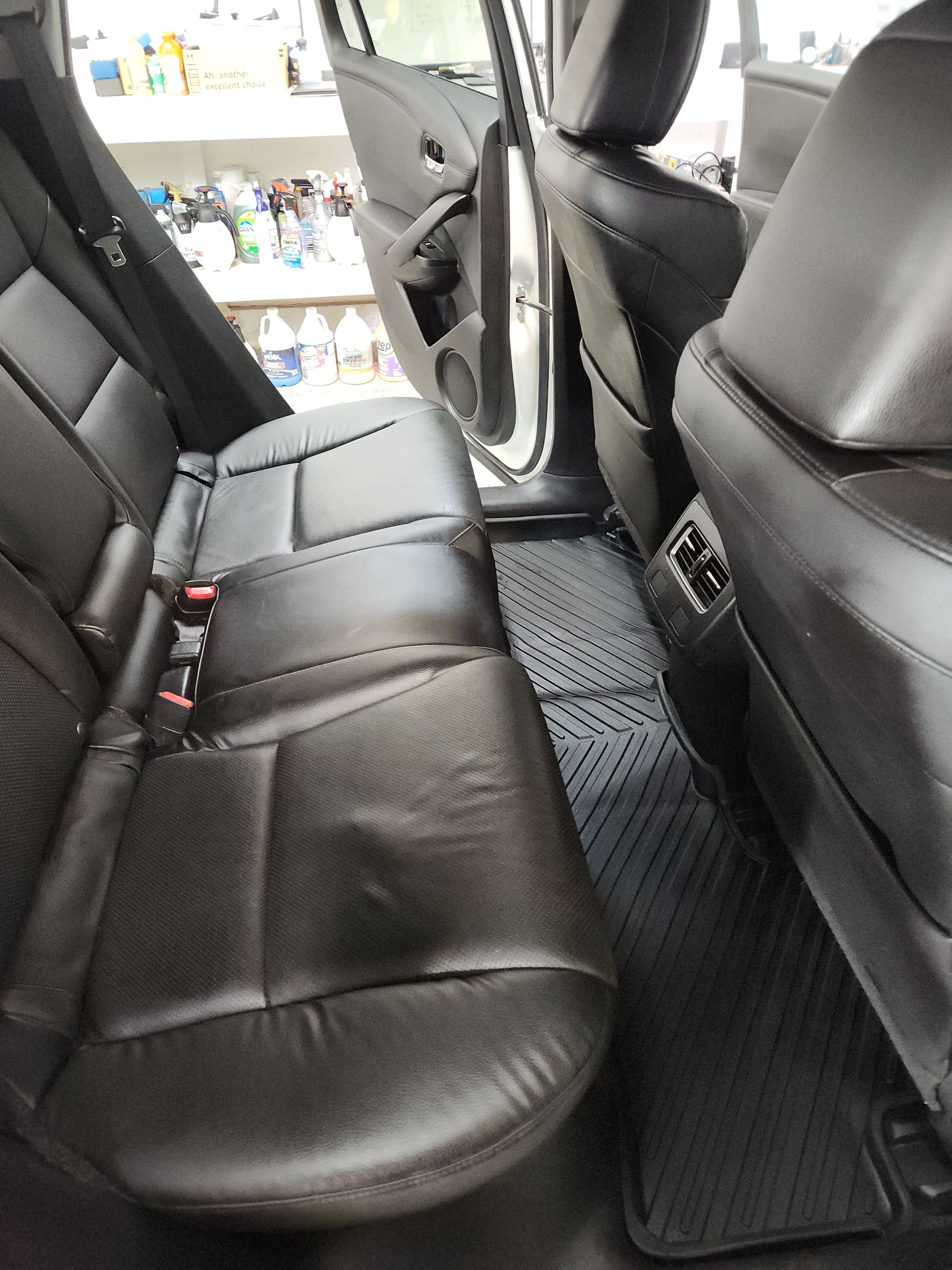 The back seat of a car with black leather seats and a black mat on the floor.