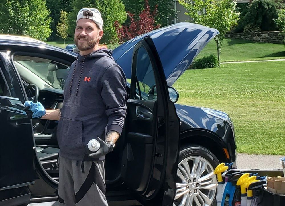 A man is standing next to a car with the hood up.