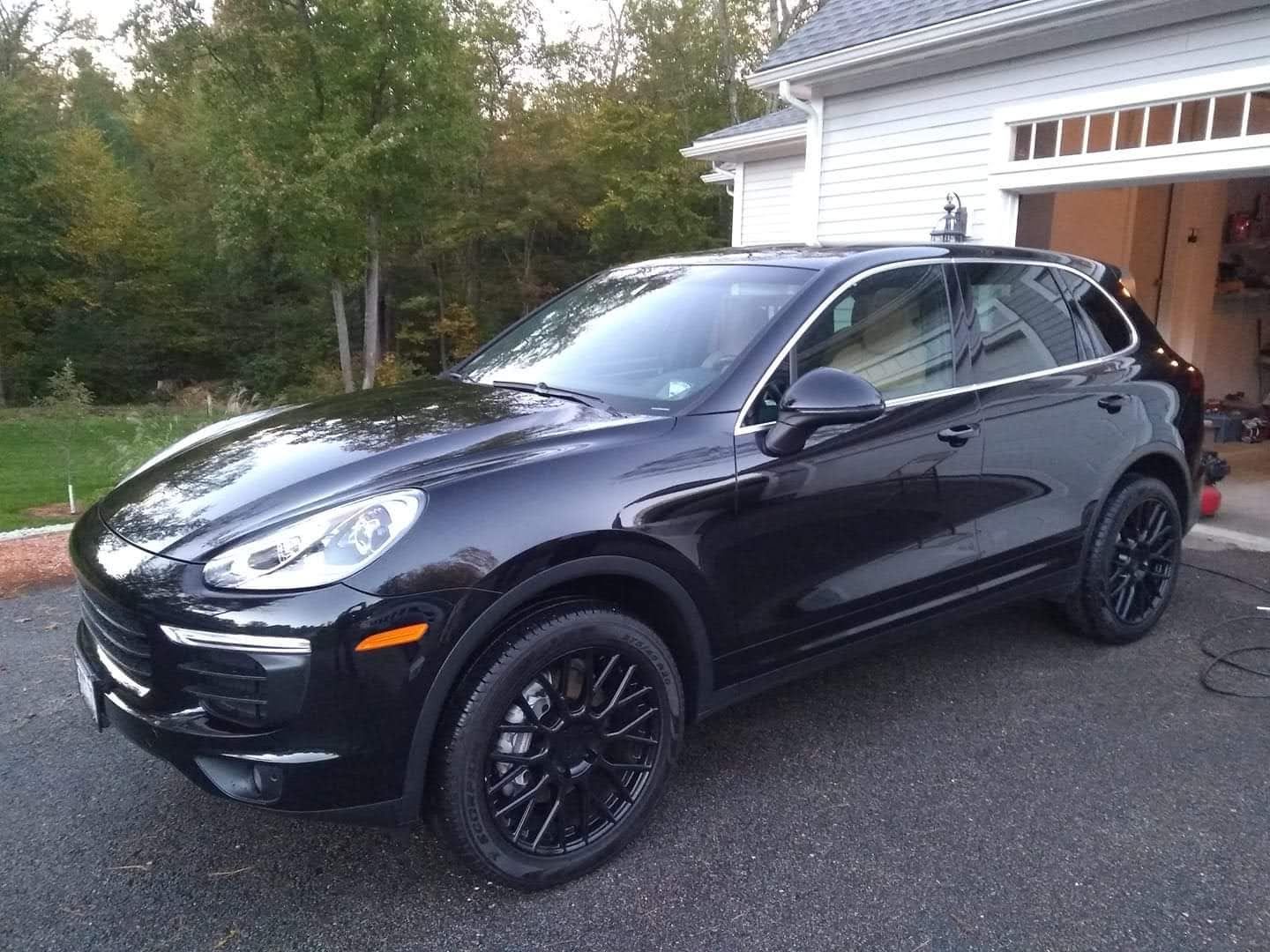 A black porsche cayenne is parked in front of a garage.