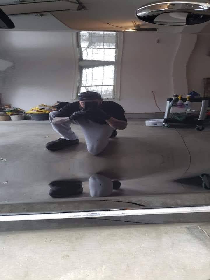 A man is kneeling down in a garage taking a picture of himself in a mirror.