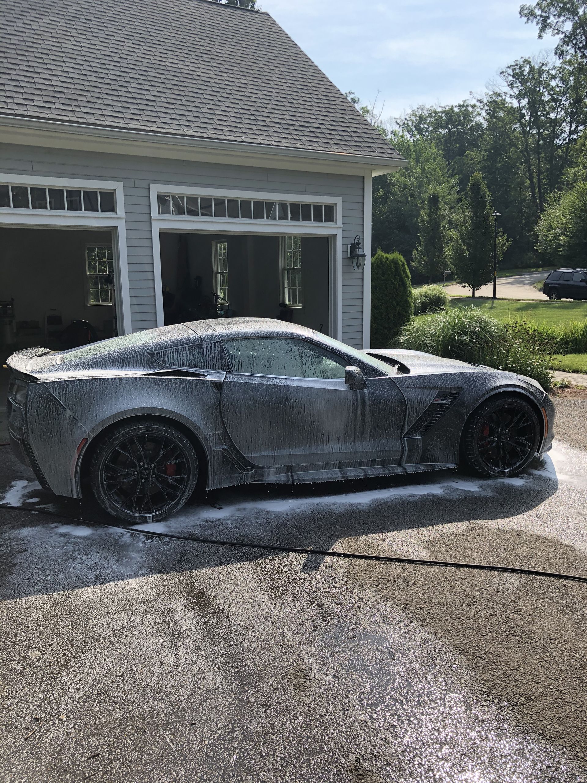 A car is covered in foam in front of a garage.