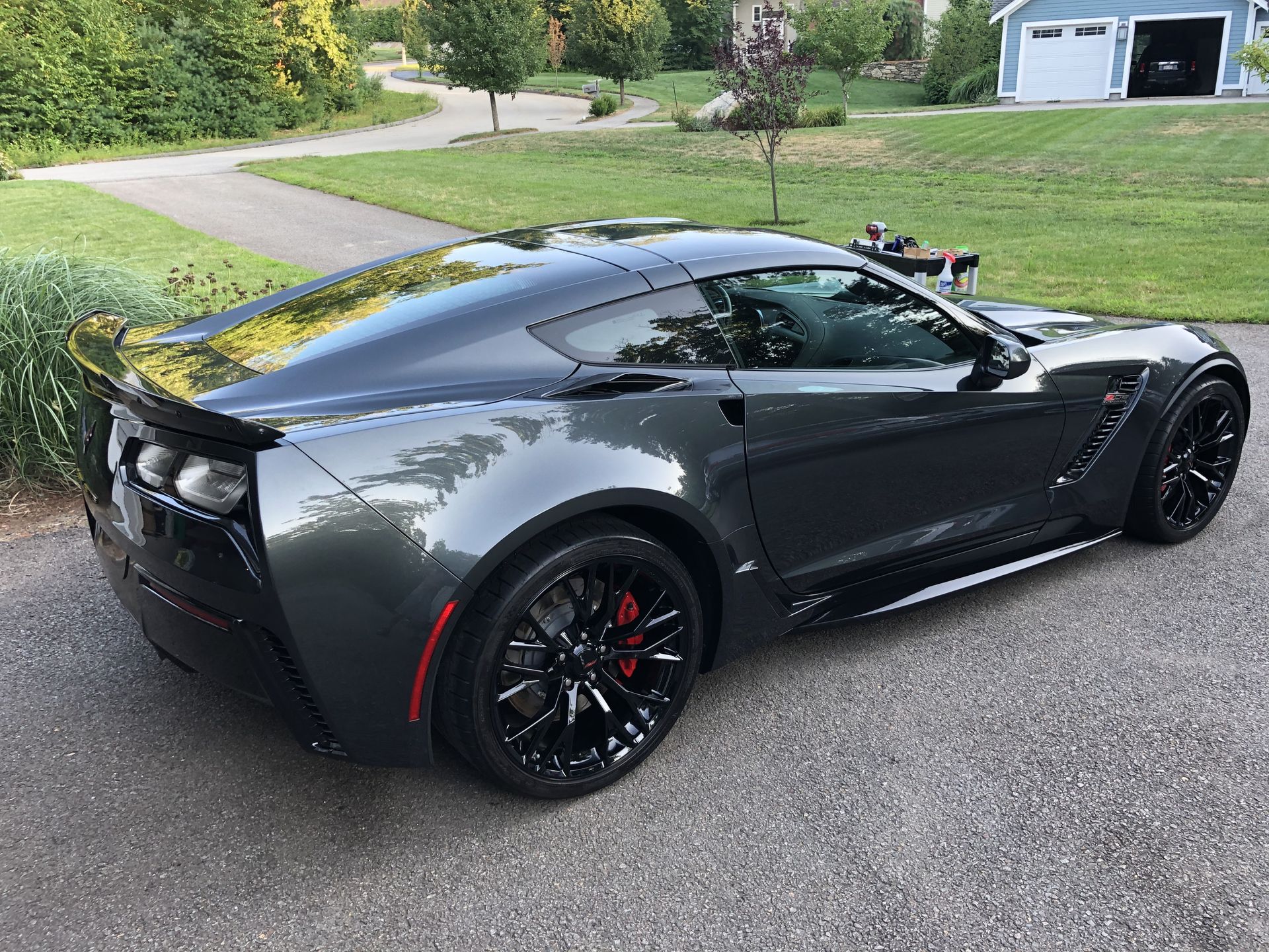 A gray sports car is parked in a driveway next to a garage.