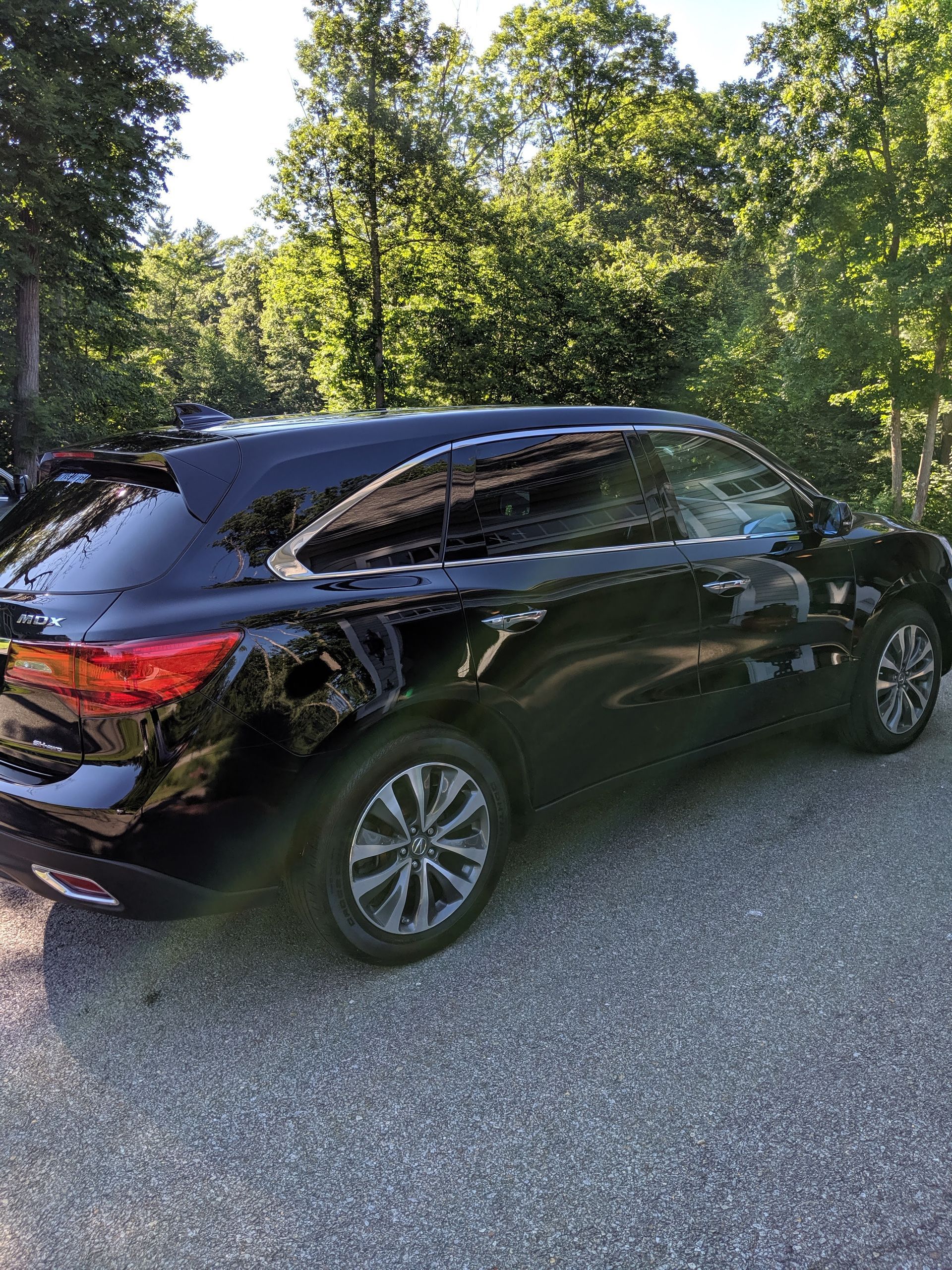 A black suv is parked in a gravel lot in front of trees.