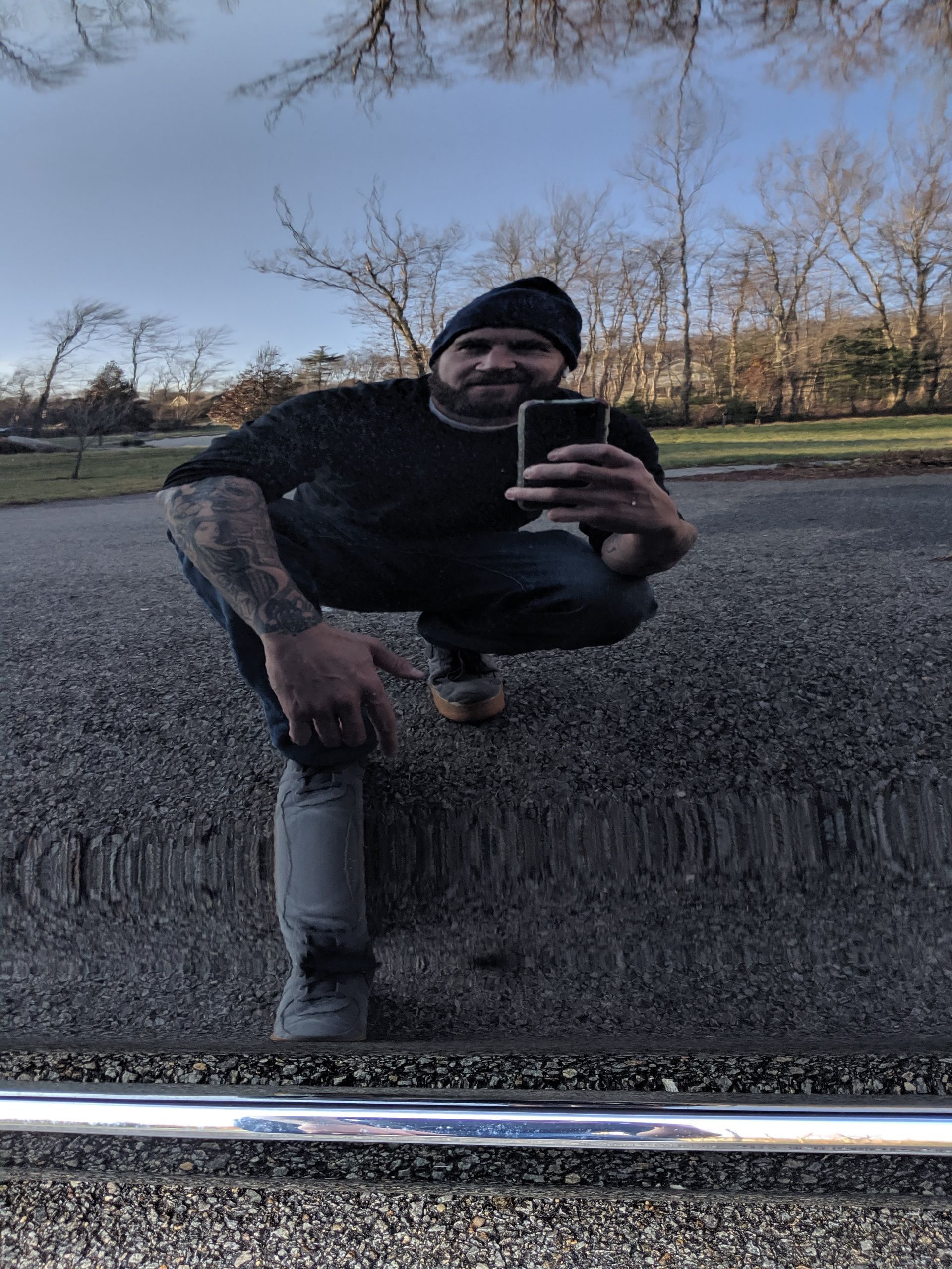 A man is squatting down and taking a picture of himself in a mirror.