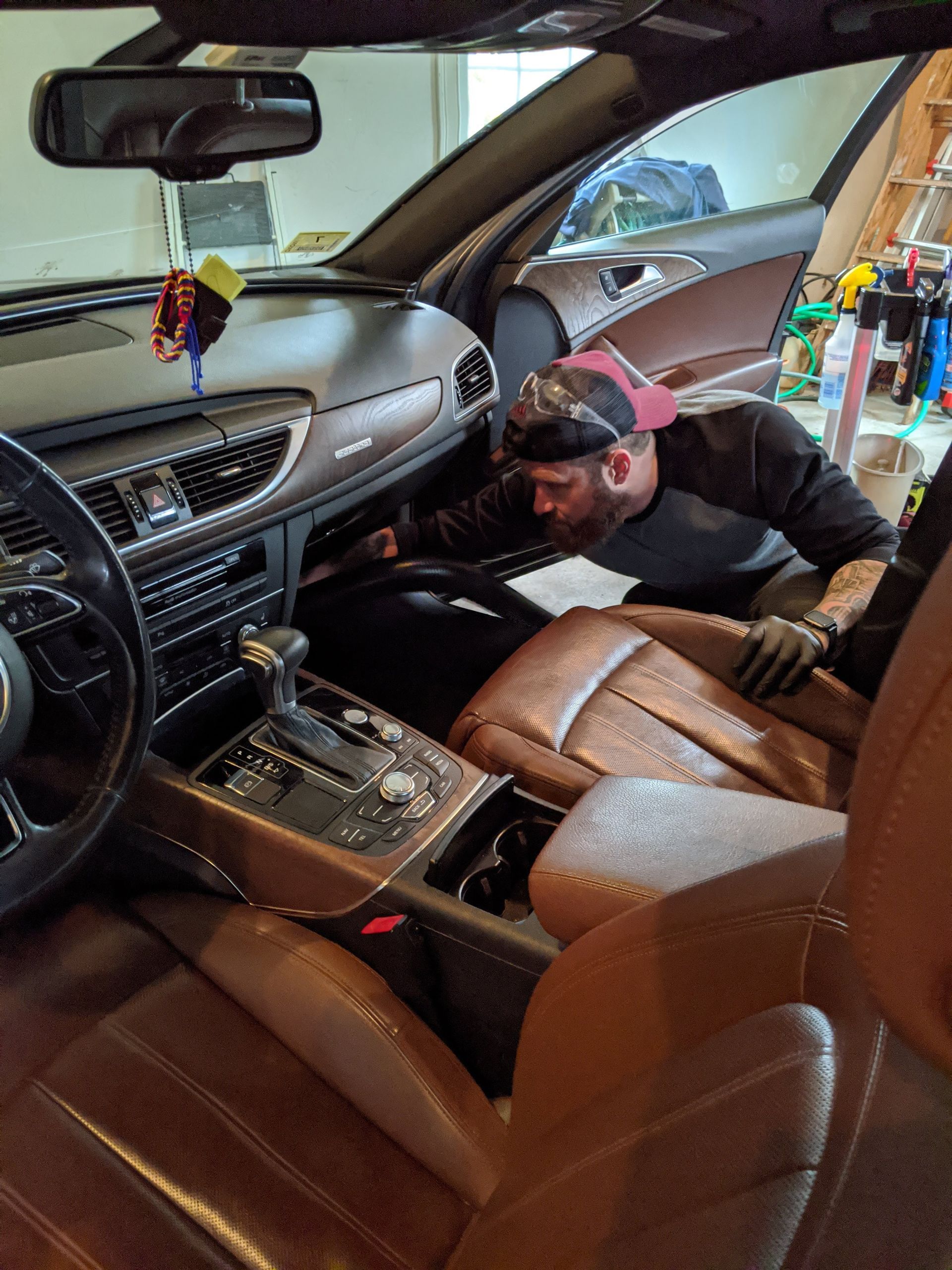 A person wearing gloves vacuums the interior of a car with brown leather seats.