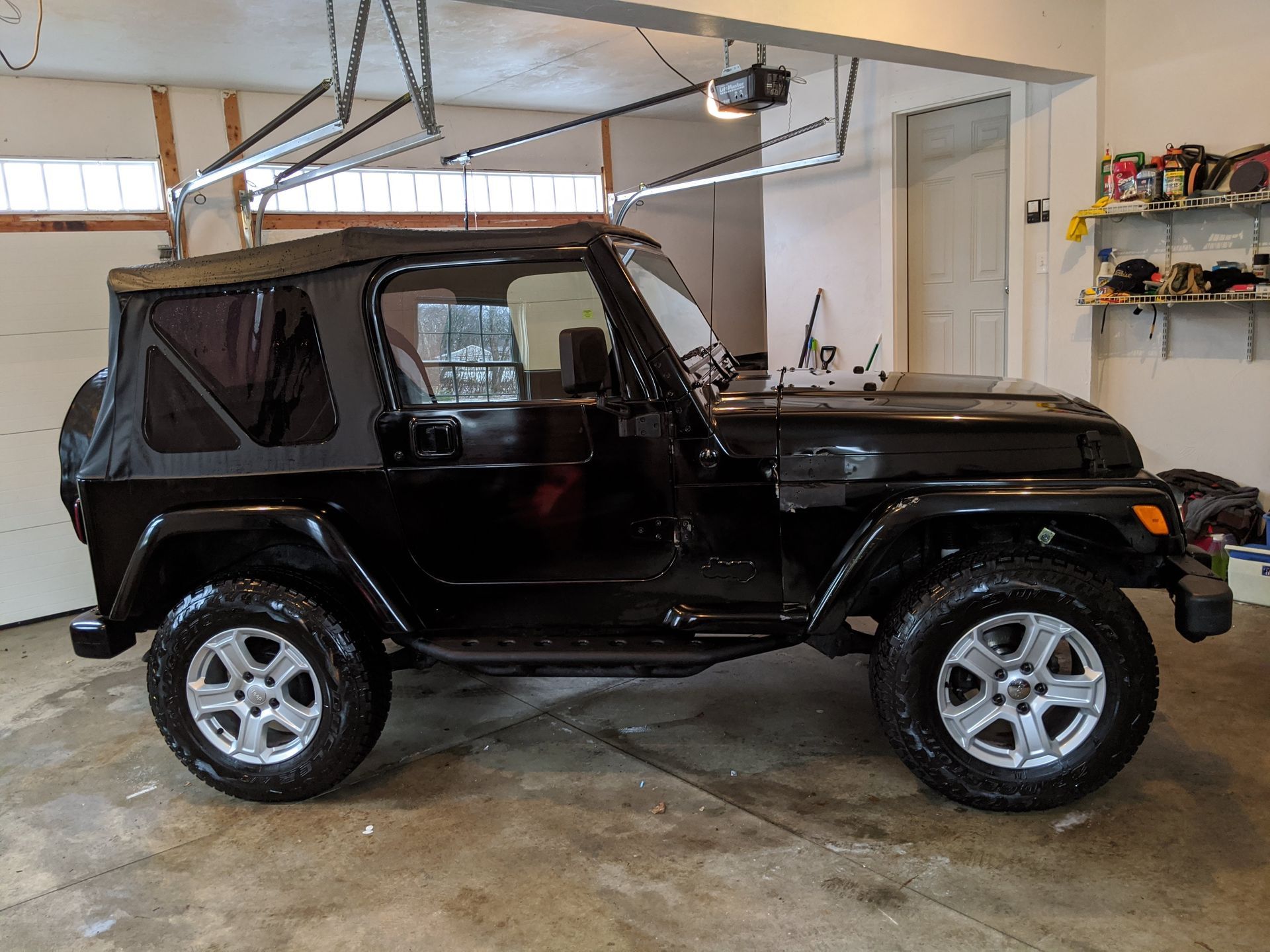 A black jeep is parked in a garage under a garage door.