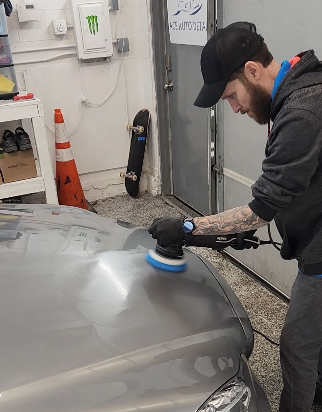 A man is polishing the hood of a car with a machine.