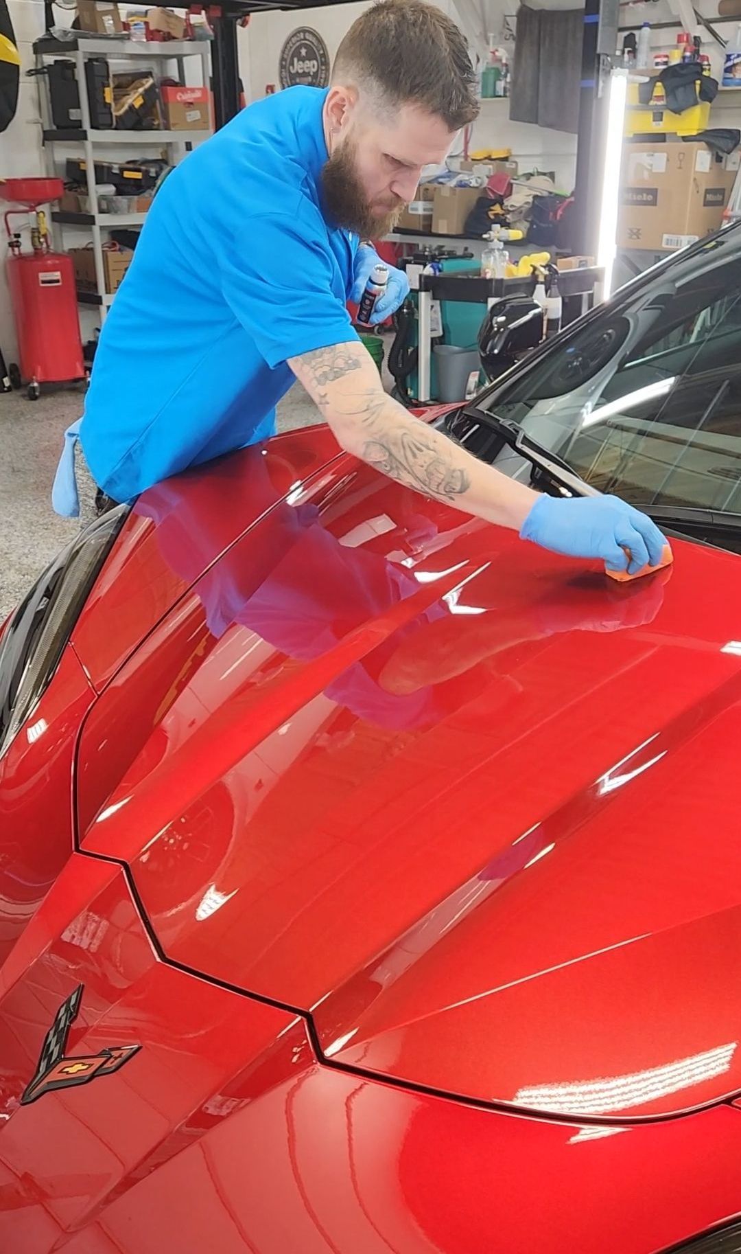 A man is polishing the hood of a red sports car.