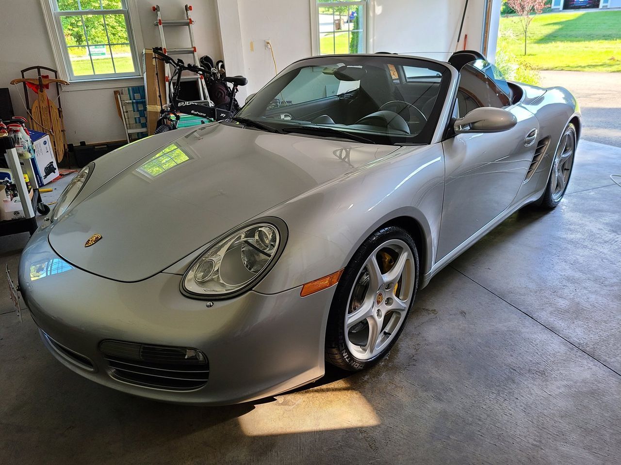 A silver porsche boxster is parked in a garage.