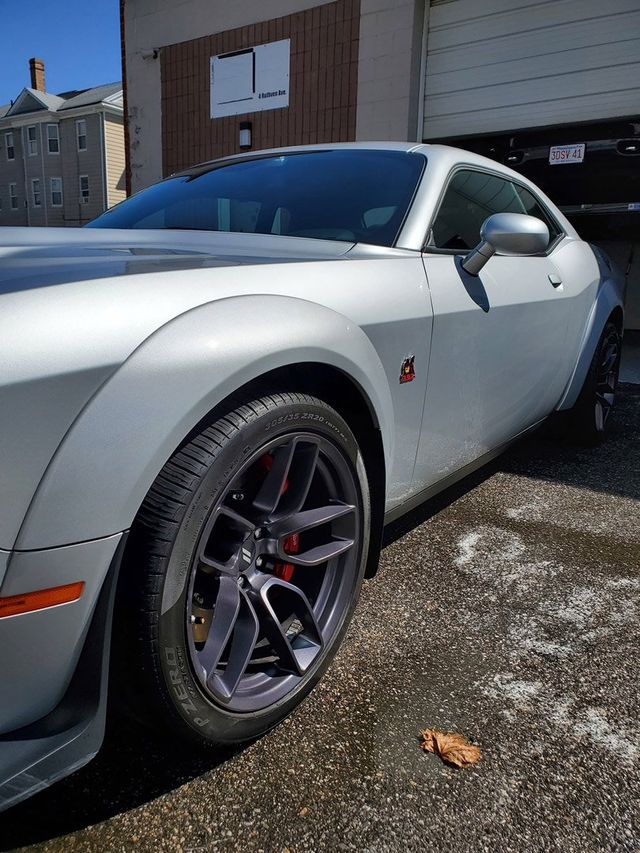A silver dodge challenger is parked in front of a garage.