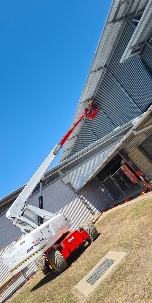 A red and white crane is sitting in front of a building putting up bird proofing devices