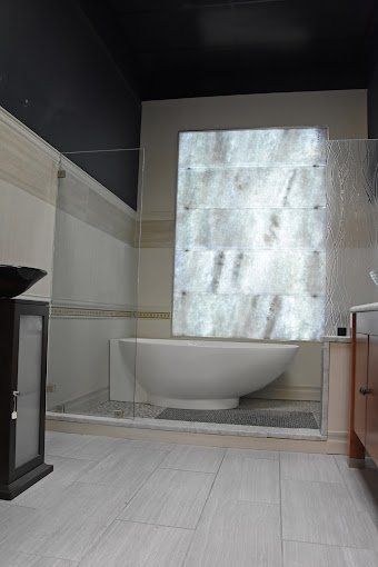 Modern bathroom with a white oval tub, glass shower wall, and stone tile floors.