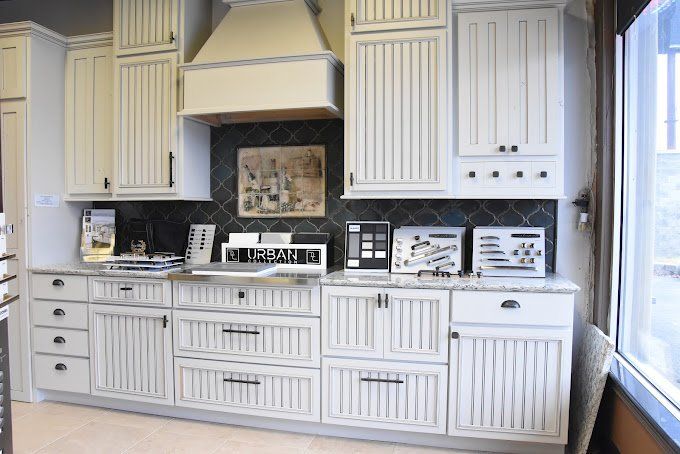 White kitchen cabinets with black hardware and a range hood against a dark tiled backsplash.