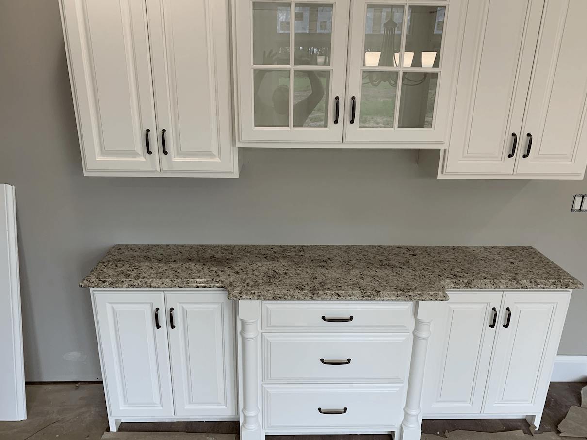 White kitchen cabinets with granite countertop against a gray wall.
