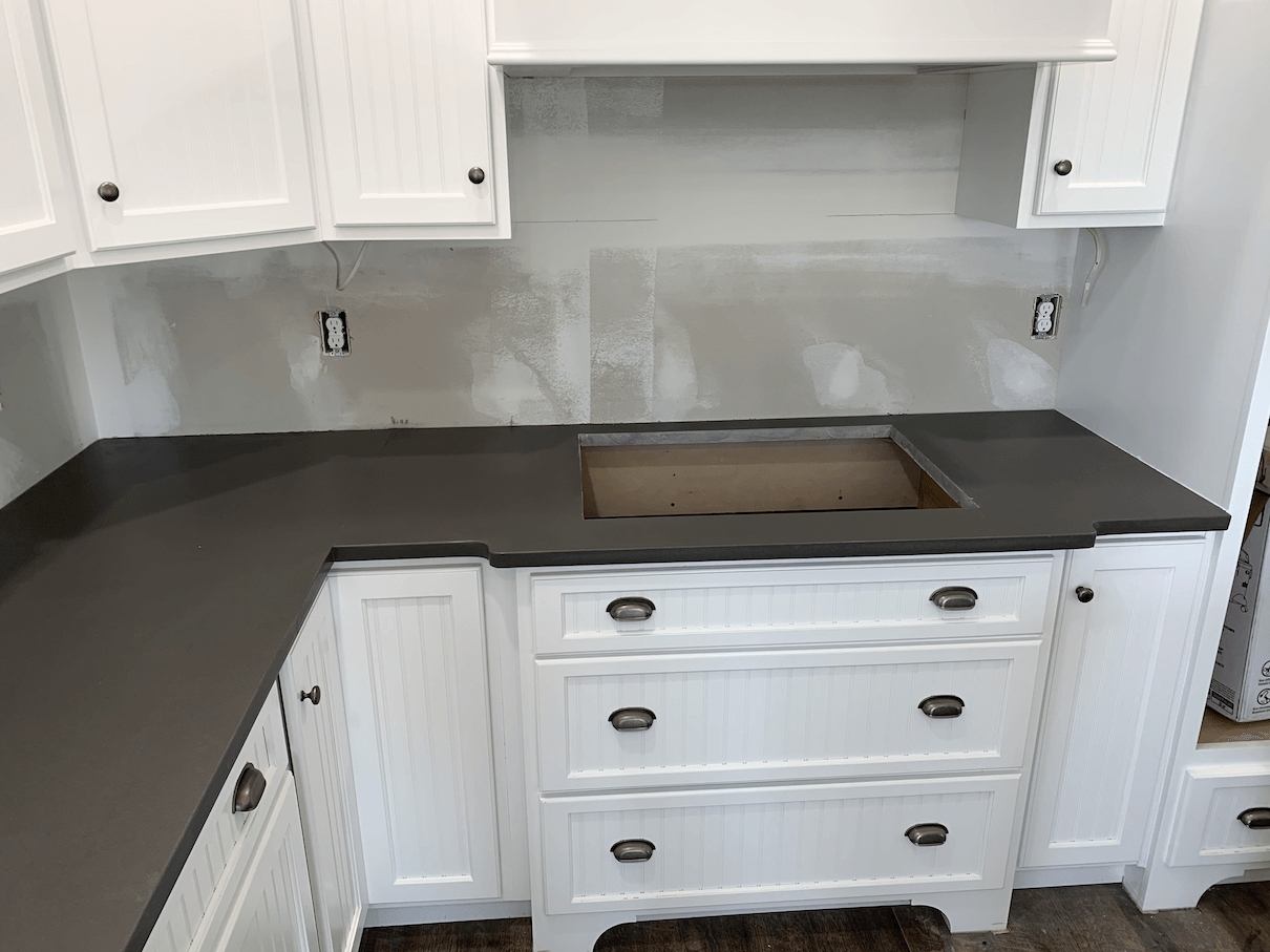 Kitchen with gray countertop, white cabinets, and empty space for a cooktop.