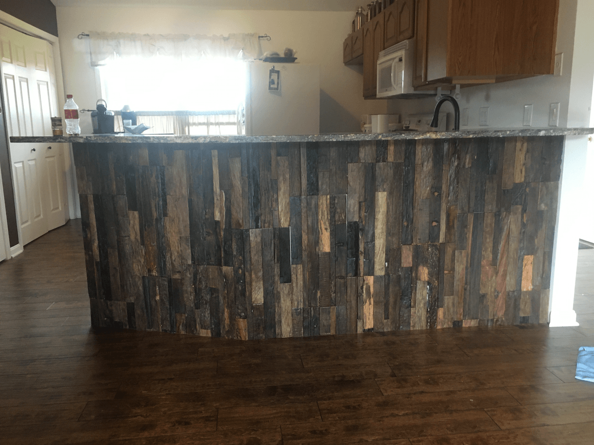 Kitchen island with weathered wood paneling, granite countertop, and microwave above.