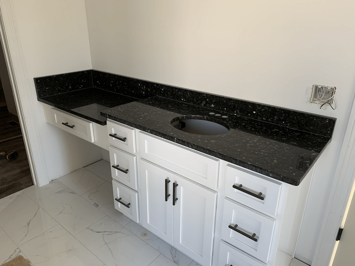 White bathroom vanity with black speckled countertop and two sinks.