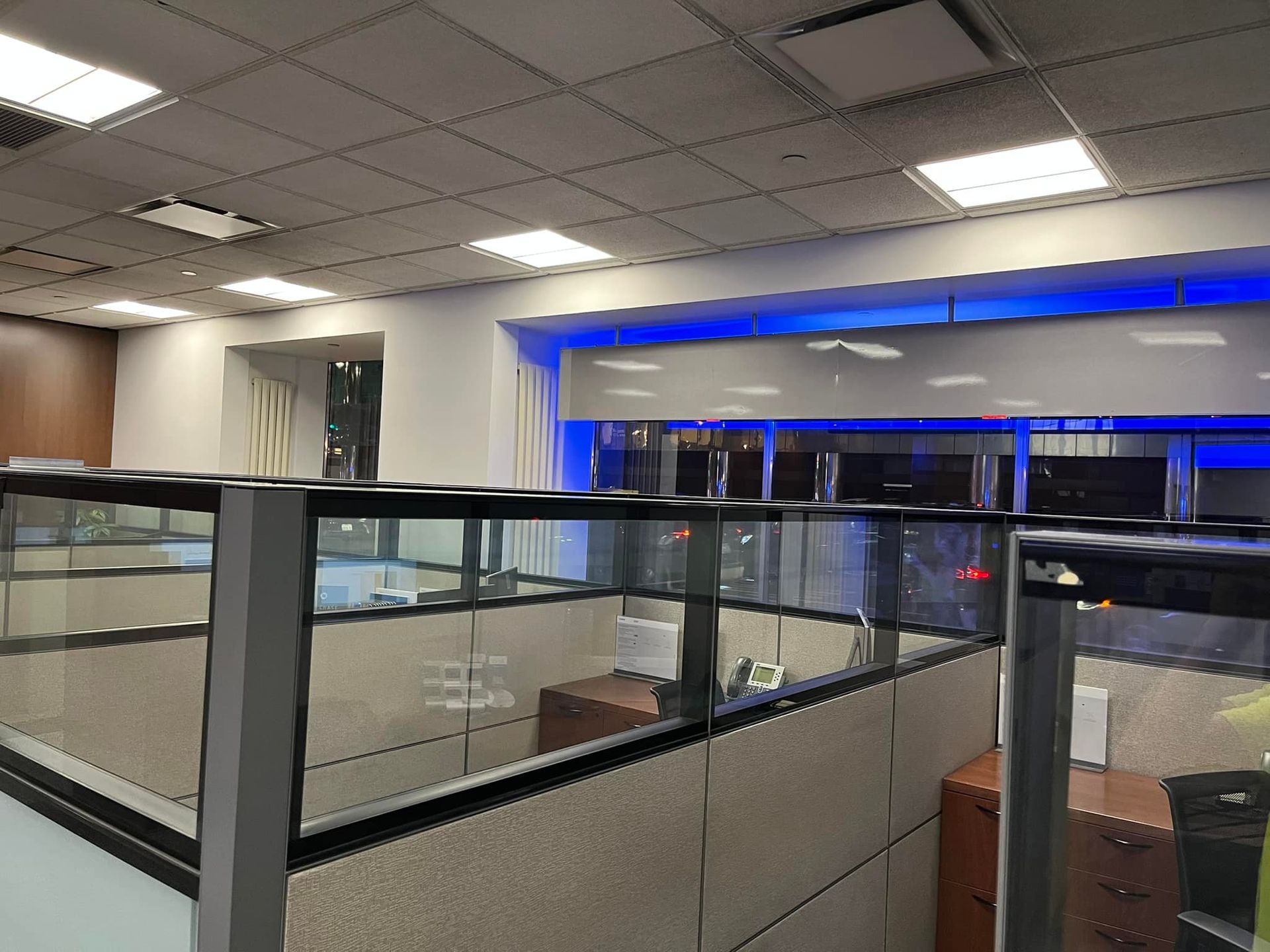 Office cubicles with glass partitions, overhead lighting, and blue accent lights on the walls.