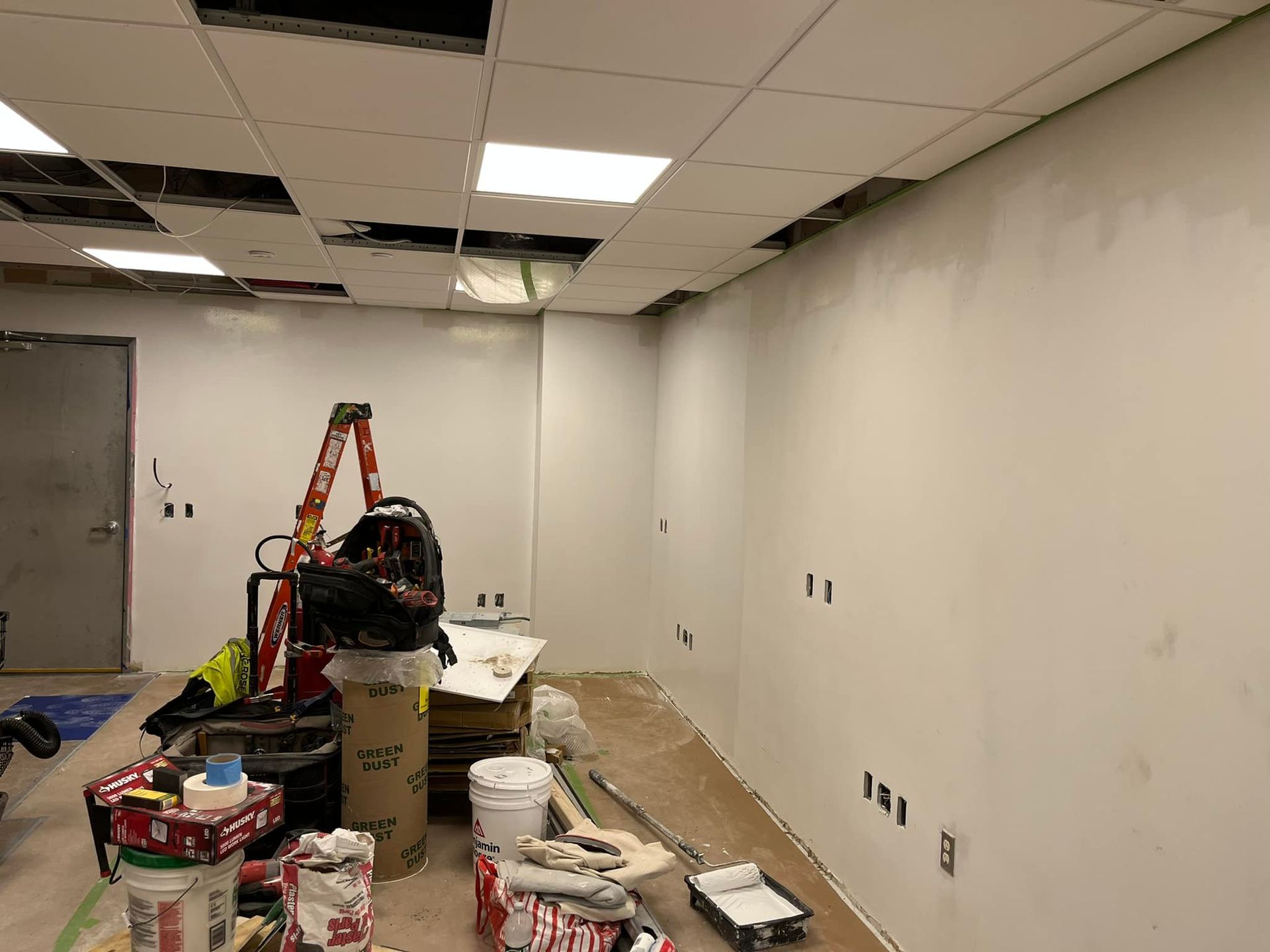 Room under construction with white walls, unfinished ceiling, and tools.