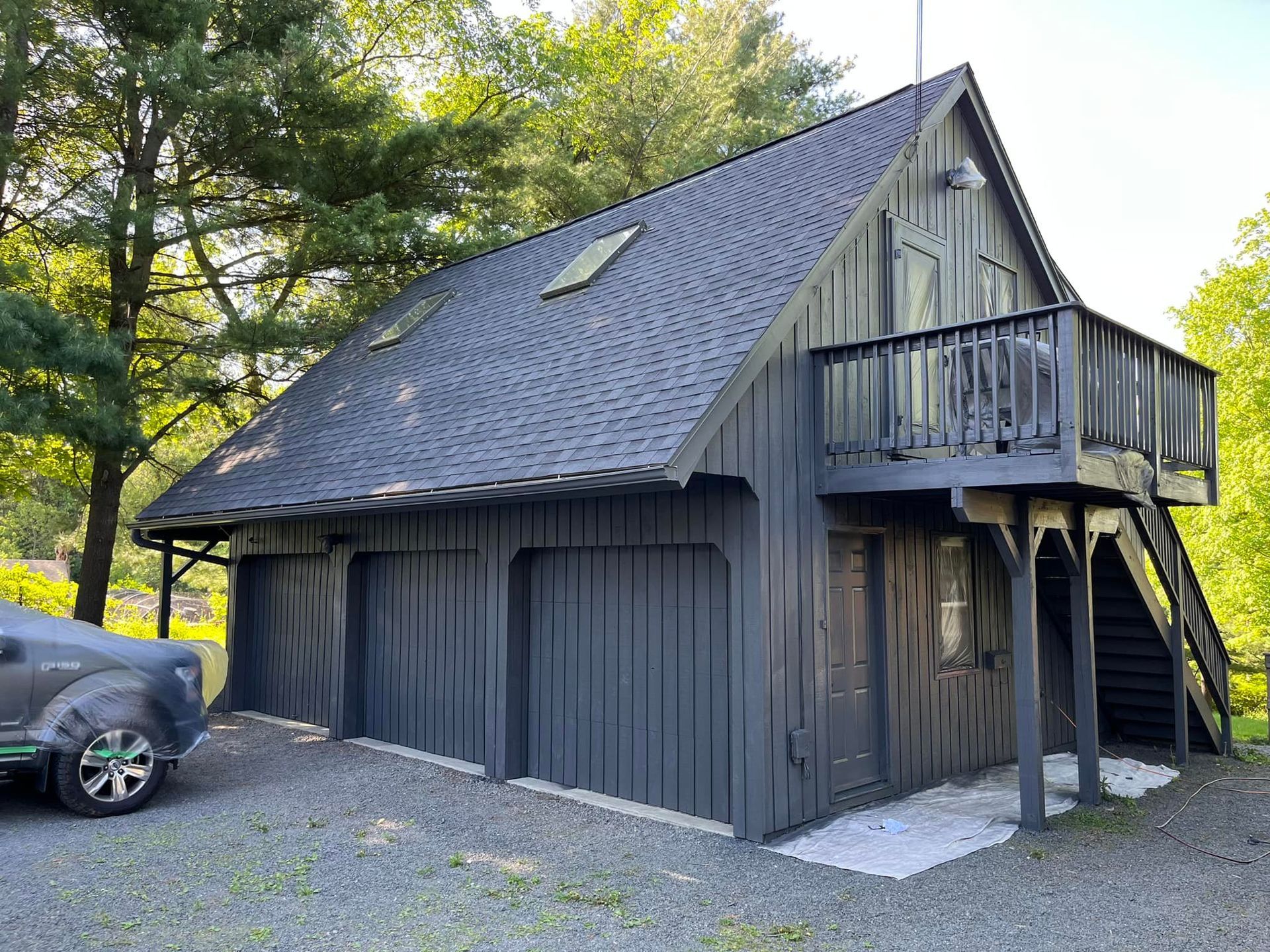 Black two-car garage with a balcony and outdoor stairs; a gray pickup truck is parked in the driveway.