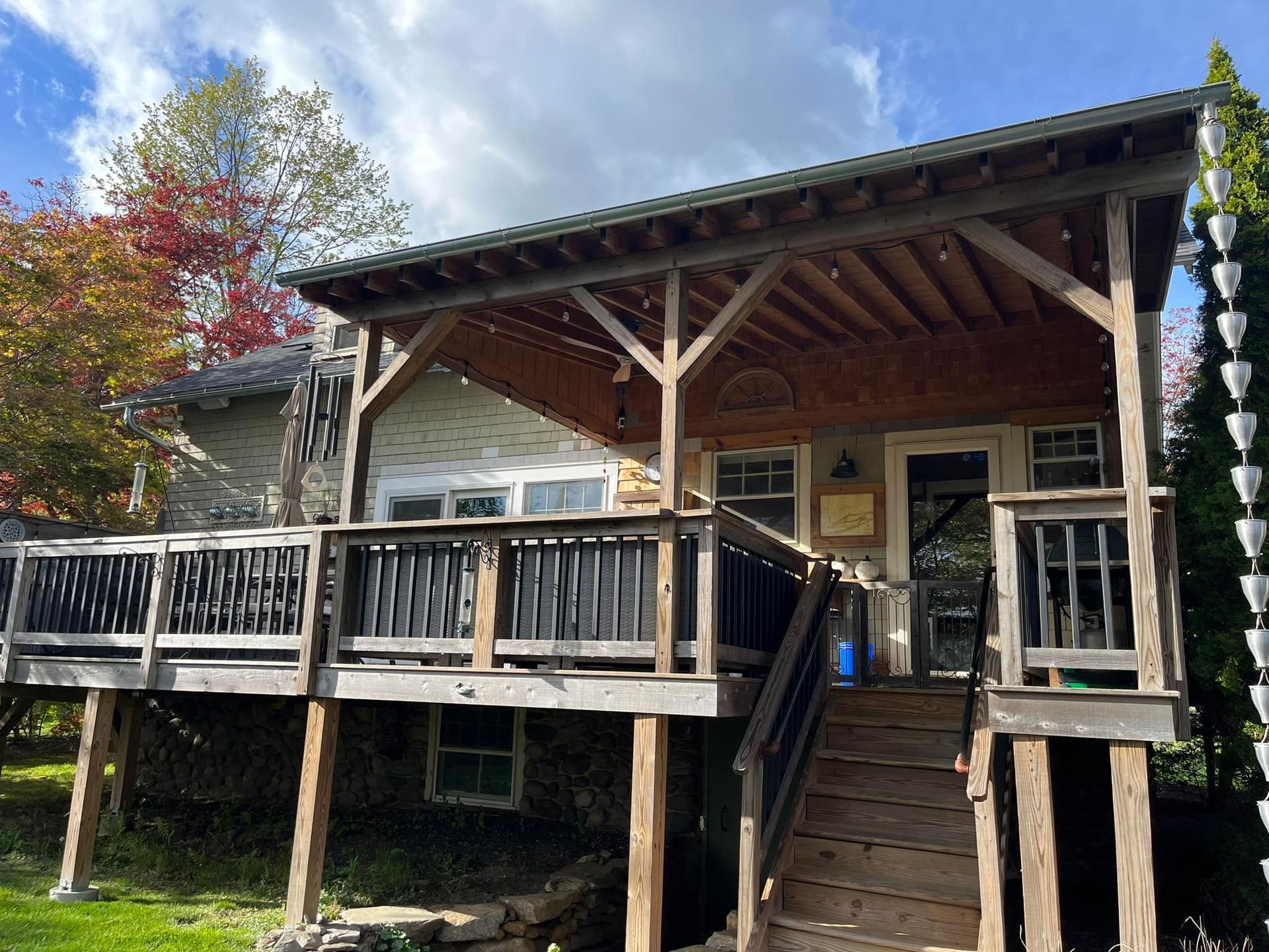 Wooden house with deck and covered porch, green roof, autumn trees.