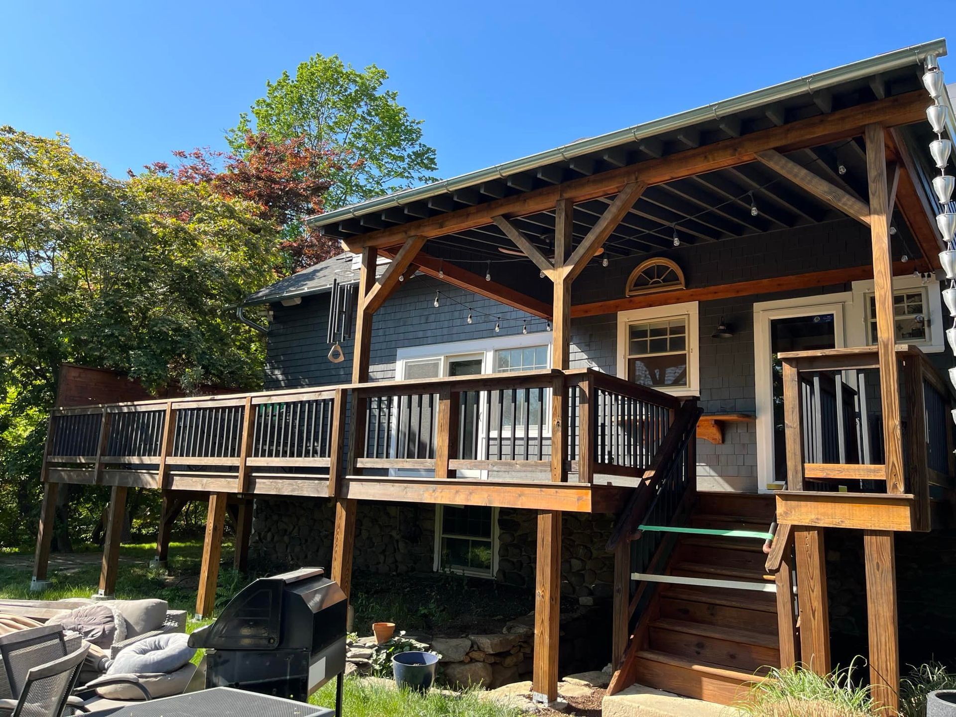 Wooden deck and patio attached to a gray house, with a grill on the lower level.