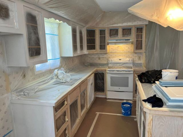 A kitchen under renovation with taped-off white cabinets, a white stove, and protective plastic sheets covering surfaces.