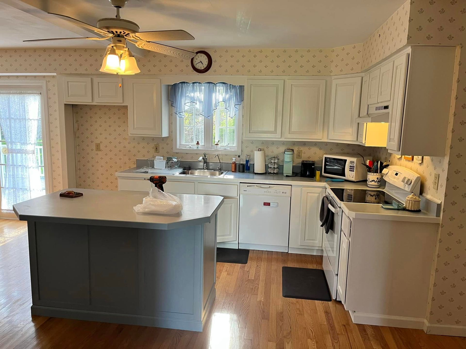 A kitchen with white cabinets, a gray island, and wooden floors. A sliding glass door is on the left.