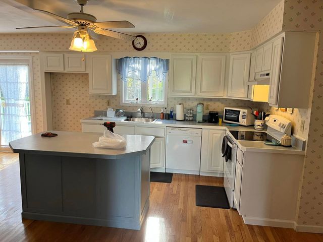 A kitchen featuring white cabinets, a gray island, light wood floors, and patterned wallpaper.