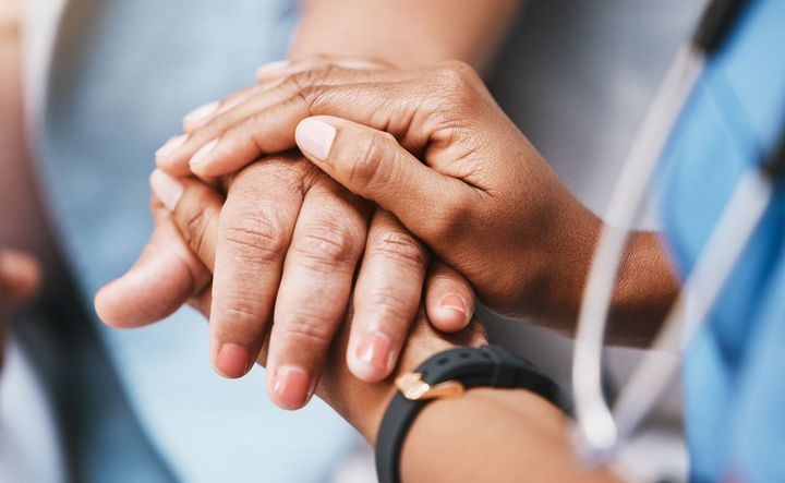 A nurse is holding the hand of an elderly woman.