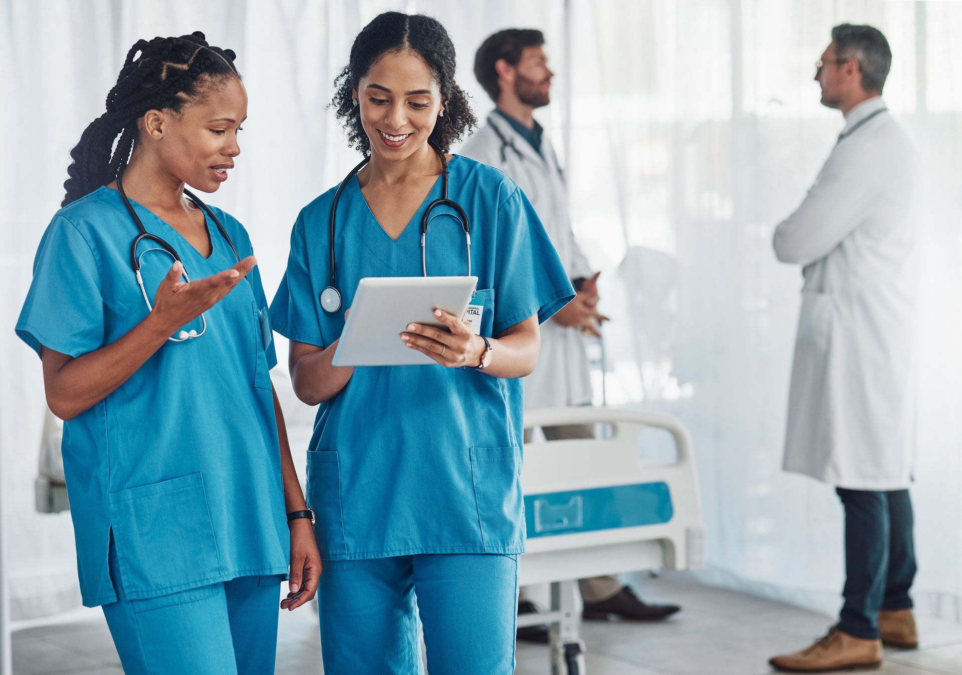 A group of doctors and nurses are standing in a hospital room looking at a tablet.