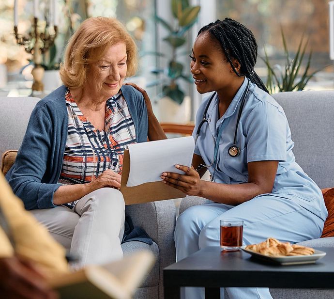 A nurse is talking to an elderly woman while sitting on a couch.