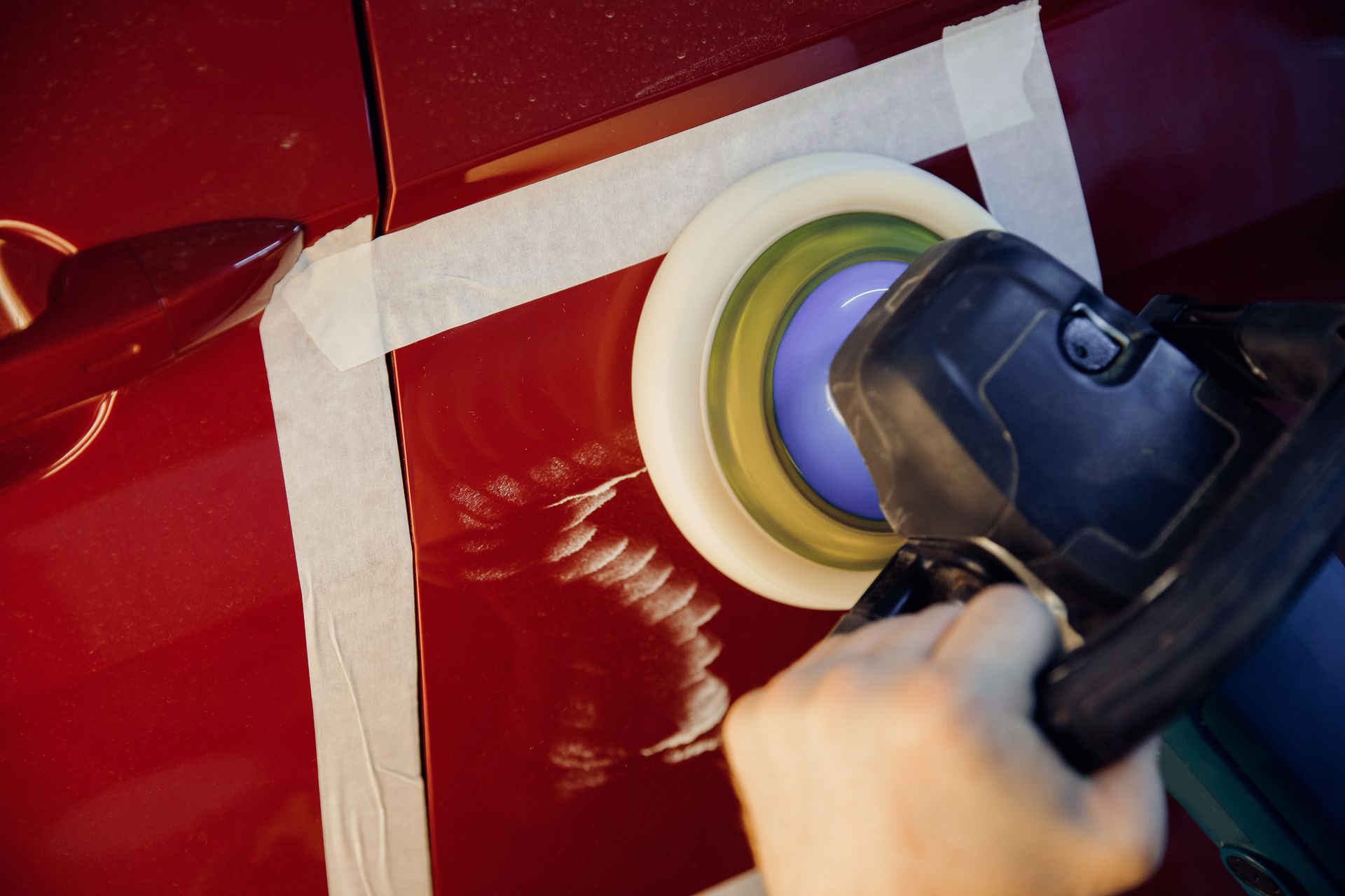 A person is polishing a red car with a machine.