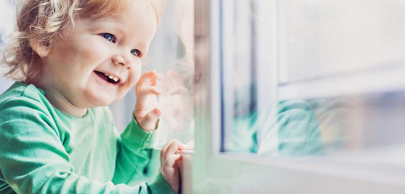 Un ragazzino guarda fuori da una finestra e sorride.
