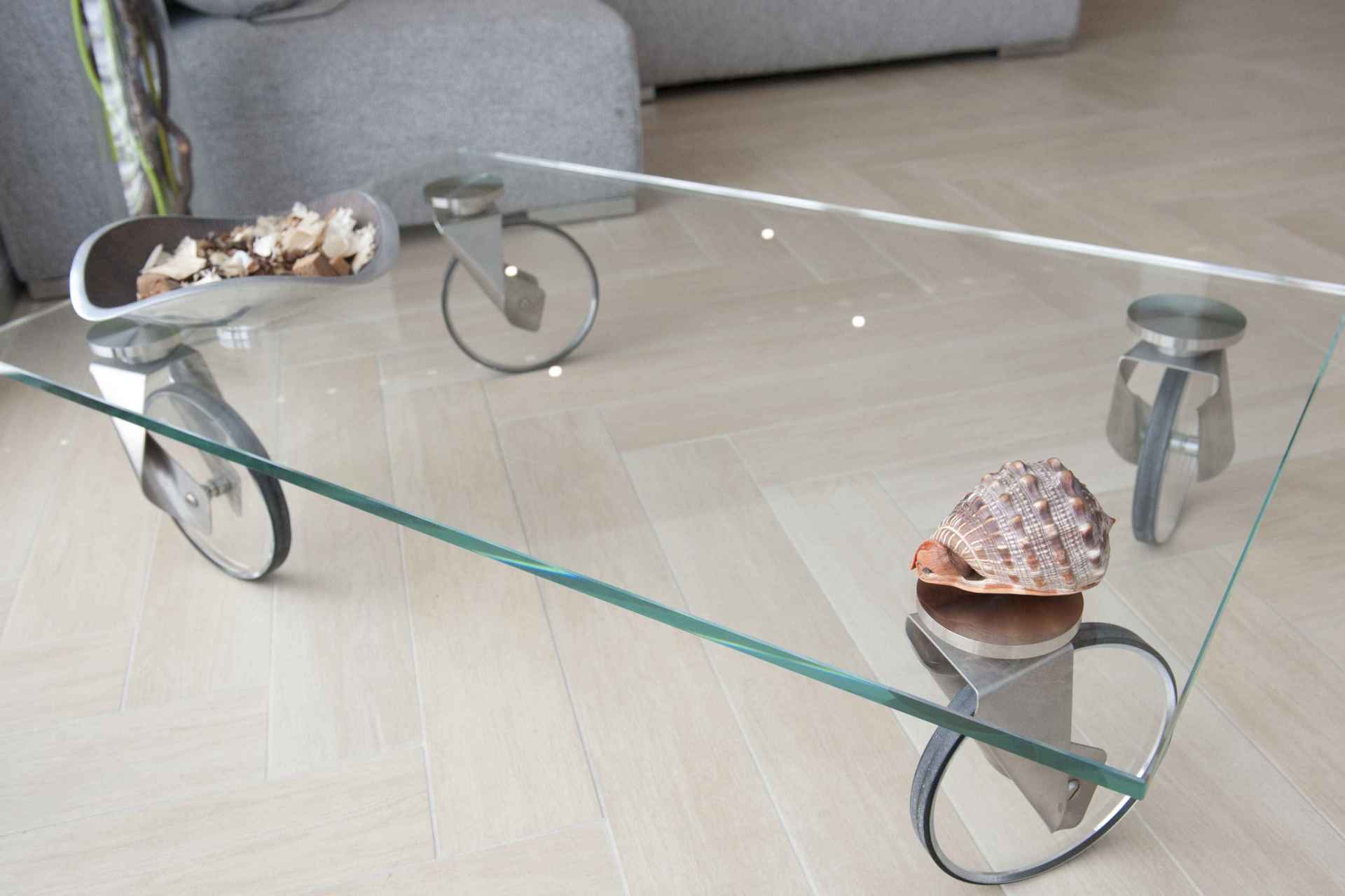 Un tavolino in vetro con ruote è appoggiato su un pavimento in legno