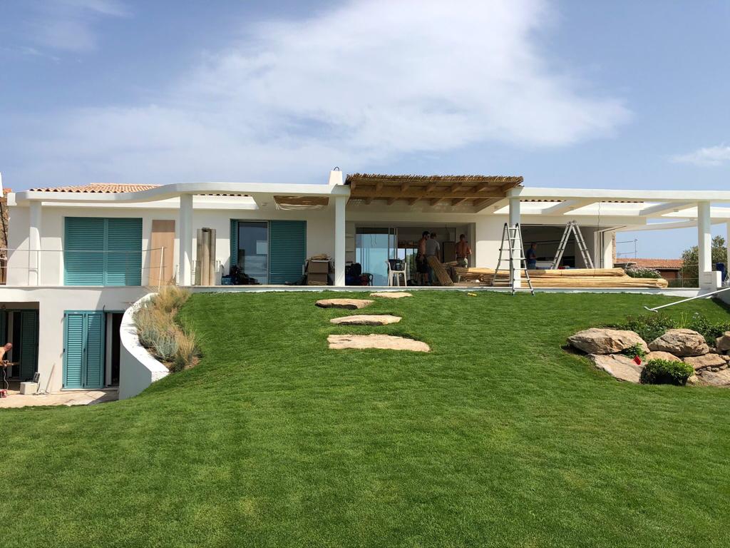 Una grande casa bianca è situata in cima a una collina verde lussureggiante.