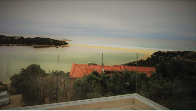 Vista sull'oceano da un balcone con ringhiera in vetro.