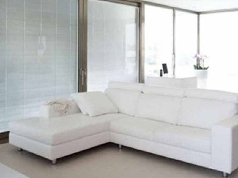 Un divano componibile bianco è seduto in un soggiorno accanto a una finestra.