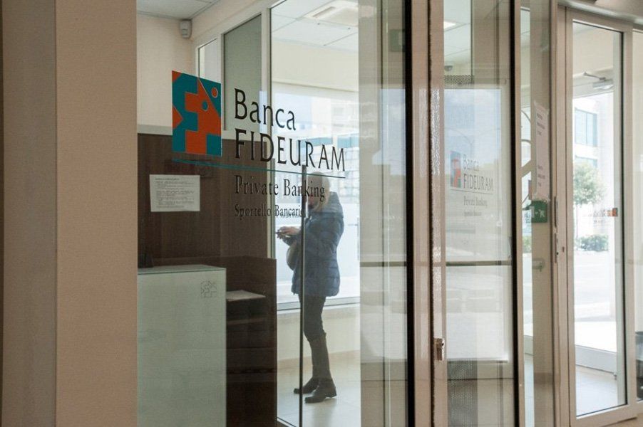 Una donna è in piedi davanti alla porta di vetro di una banca e parla al cellulare.