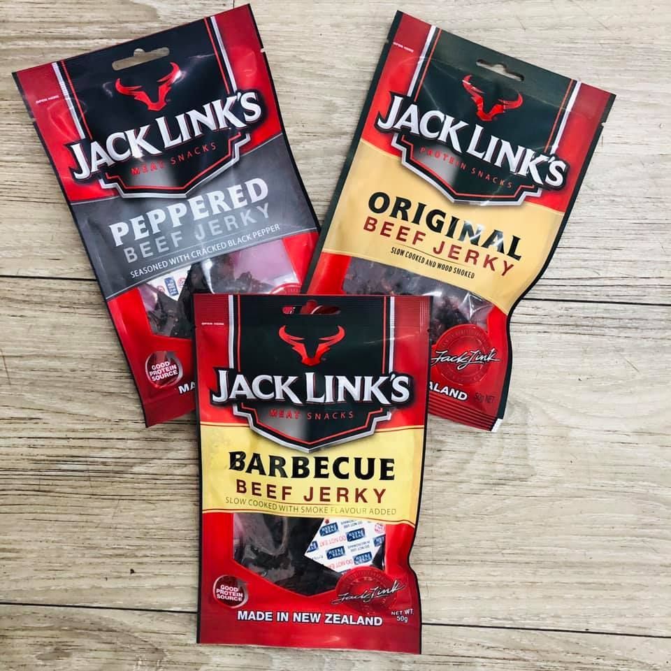 Three bags of jack links beef jerky are sitting on a wooden table.