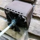 Black brush seal around a white cable passing through a brown wall vent box